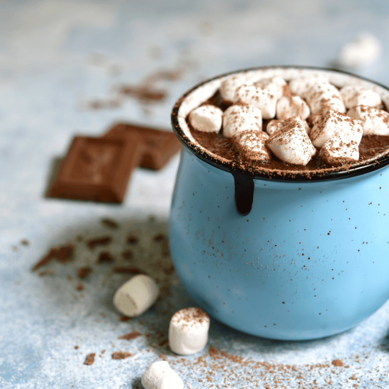 stock picture of a blue enamel mug filled with hot chocolate and dripping with small marshmallows