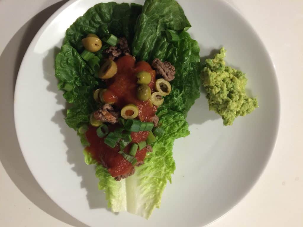 my unique yummy taco recipe. A piece of romaine lettuce topped with browned ground beef, tomato sauce, chopped green onions, green olives and avocado on the side