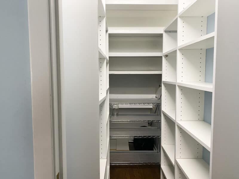 A narrow walk-in pantry with empty white shelves.