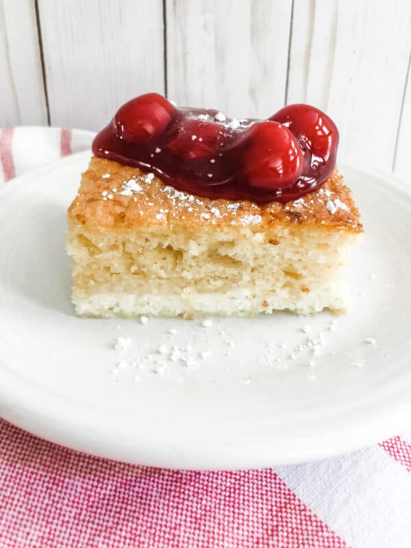 white cake on a white plate with cherry topping