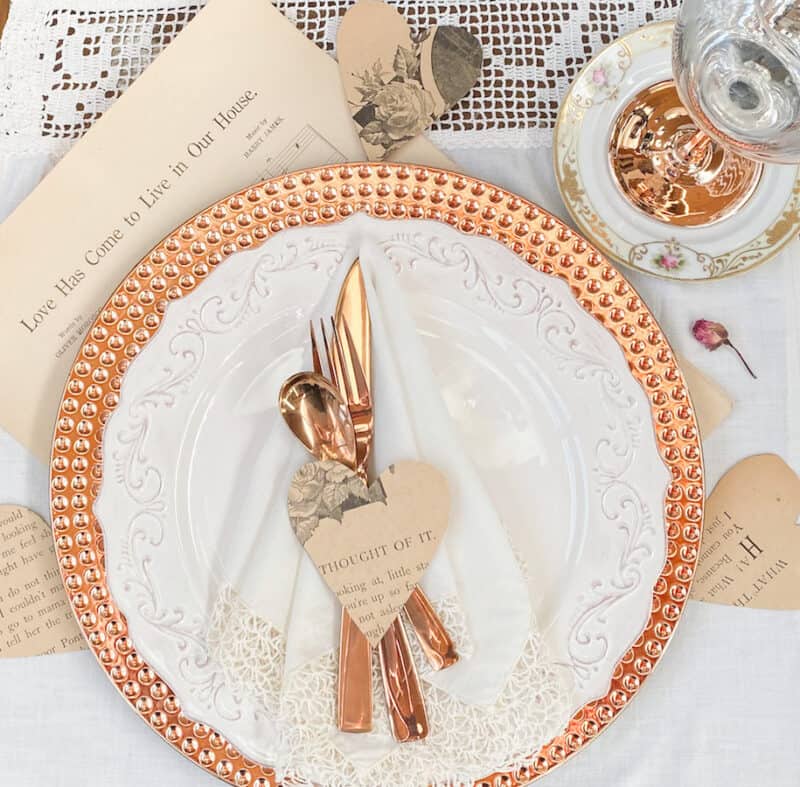 pretty Valentine's Day table with rose gold charger under a white plate, rose gold silverware and wine glass