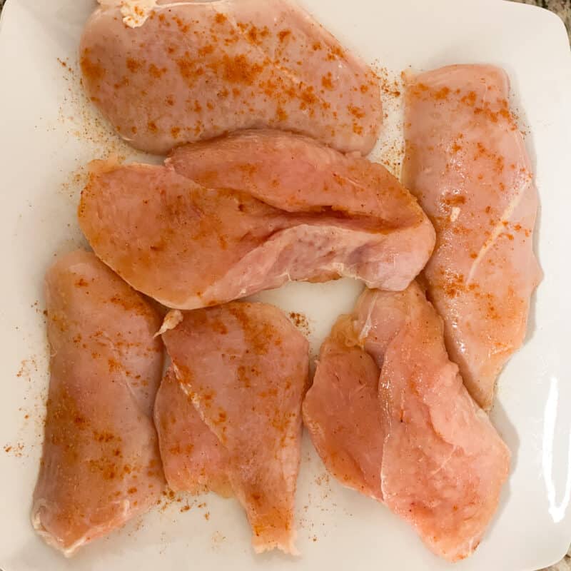 Raw butterflied Chicken Breast on white plate seasoned with olive oil and cayenne pepper, salt and pepper