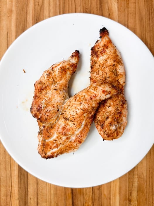 cooked cajun chicken breasts on a white plate ready to be cut and put on top of caesar salad