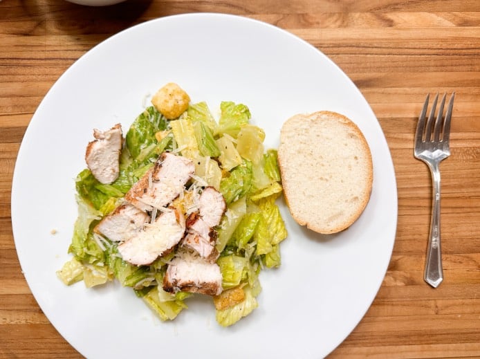 cajun chicken breast on homemade caesar salad on a white plate with a piece of french bread on the side