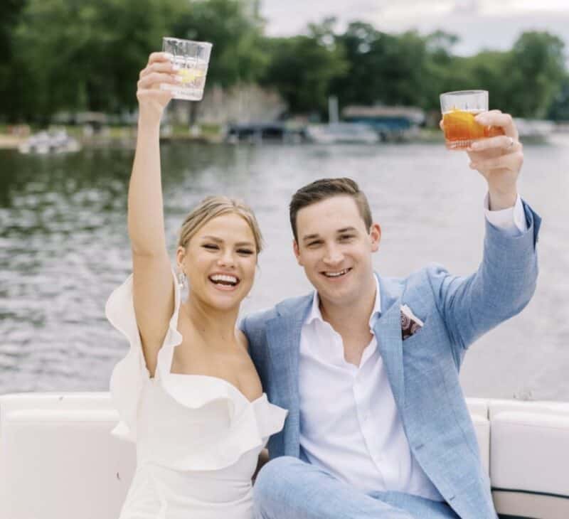 bride and groom taking a boat ride after the backyard wedding. They are sitting in the back of the moving boat, smiling with cocktails in hand, up in the air - cheers