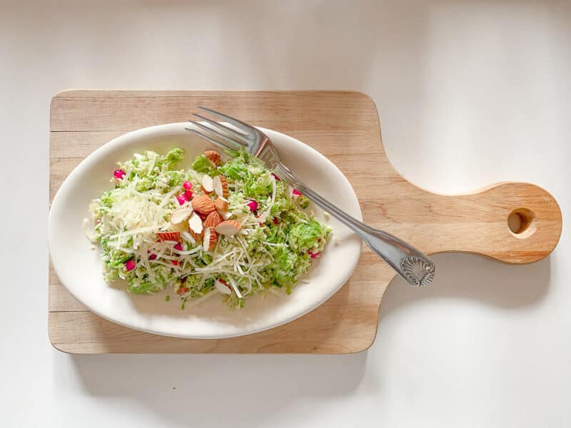 brussel sprout, pomegranate fresh fall salad on an oval plate on a wooden board with a fork