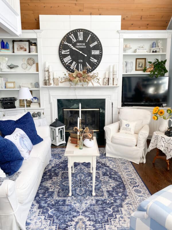 A picture of my living room with the new Walmart rug. You can see the mantel with a black clock above on the white shiplap wall. A white sofa to the left and a white chair to the right. 