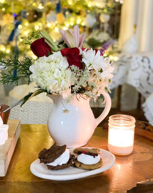 White vase with christmas flowers and a plate of s'more snack in front of tree for a quiet christmas