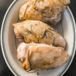 Three herb roasted bone-in chicken breasts on oval white with green striped rim dish