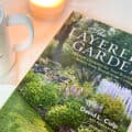 the book the layered garden on a table with a cup of coffee and a candle