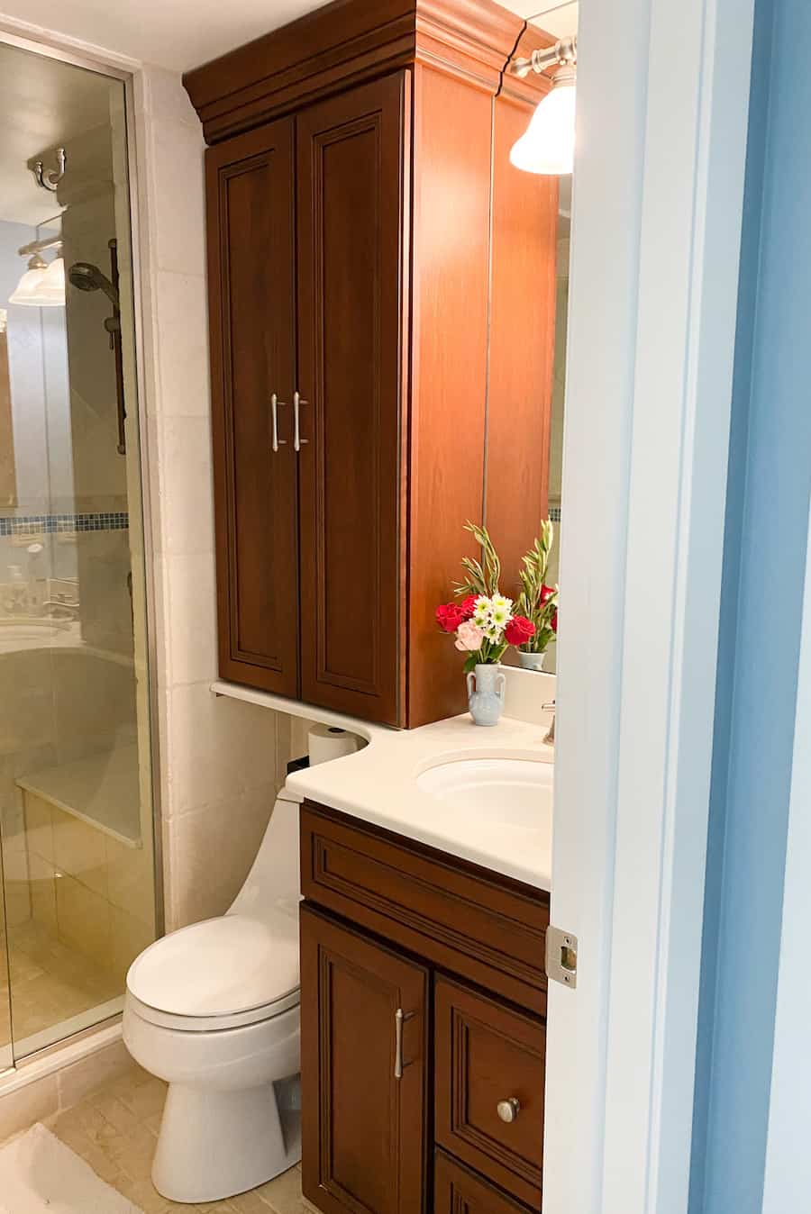 View into my small bathroom with white countertop, cherry wood cabinets and white toilet