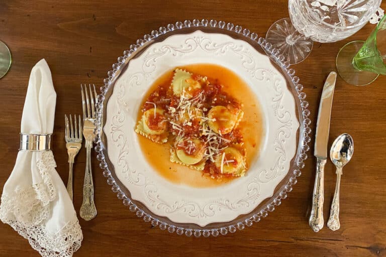 Cheesy Lobster Ravioli with Tomato Sauce on White plate with silverware, set on a dark wood table