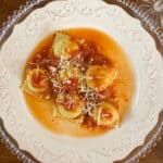 Cheesy Lobster Ravioli with Tomato Sauce on White plate, set on a dark wood table