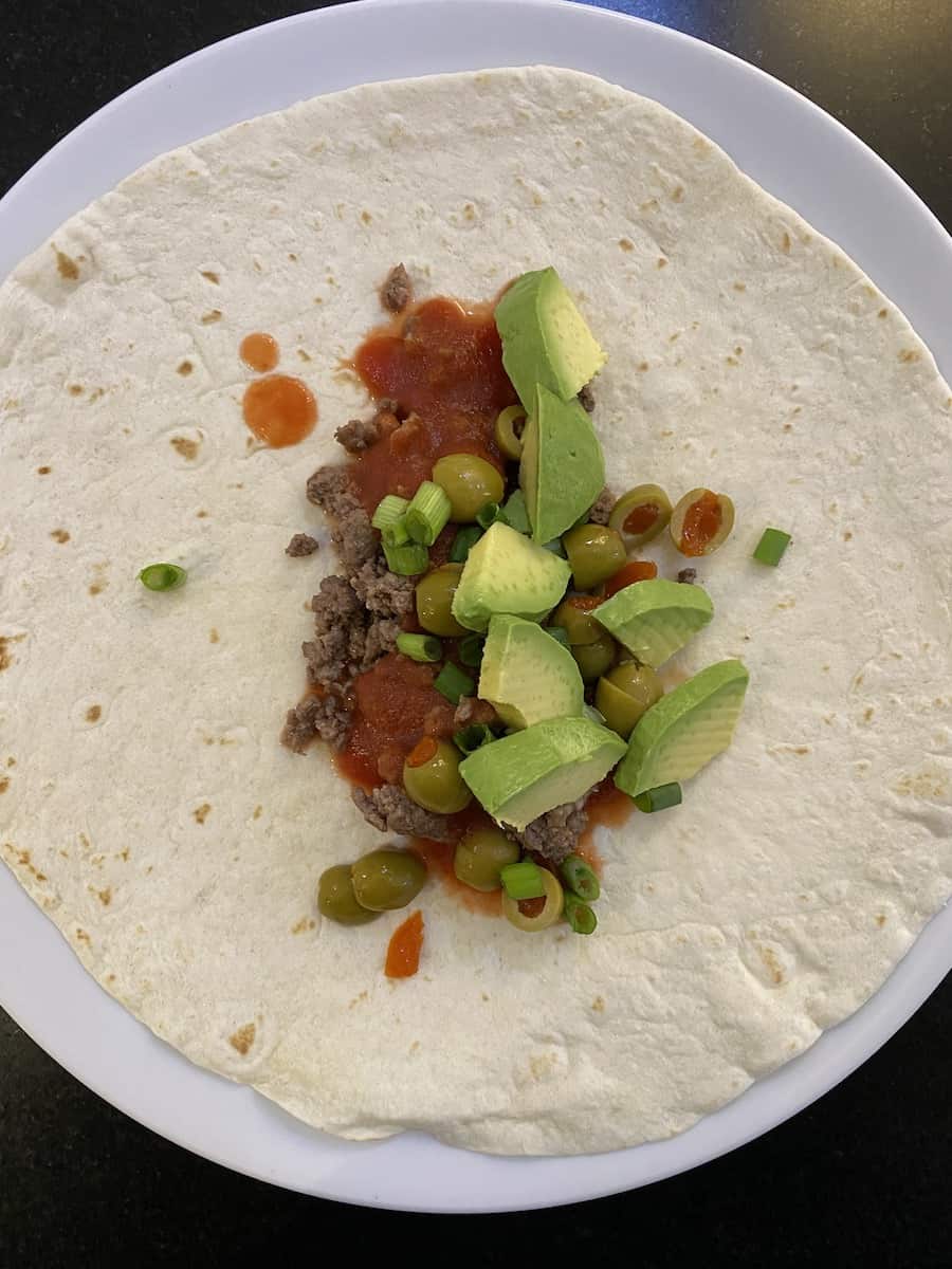 picture of my unique yummy taco recipe. flour tortillas topped with browned ground beef, tomato sauce, chopped green onions, green olives and avocado