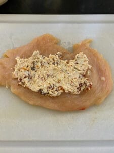 flattened chicken breast laying flat with the filling spread over the breast