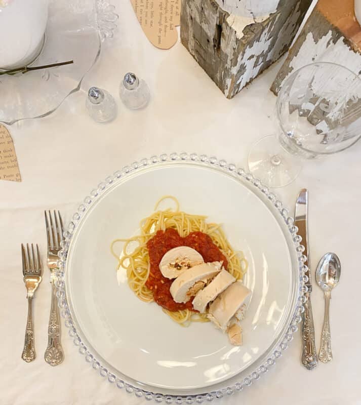 stuffed chicken breast over spaghetti and marinara sauce on a white plate set on a table ready for dinner