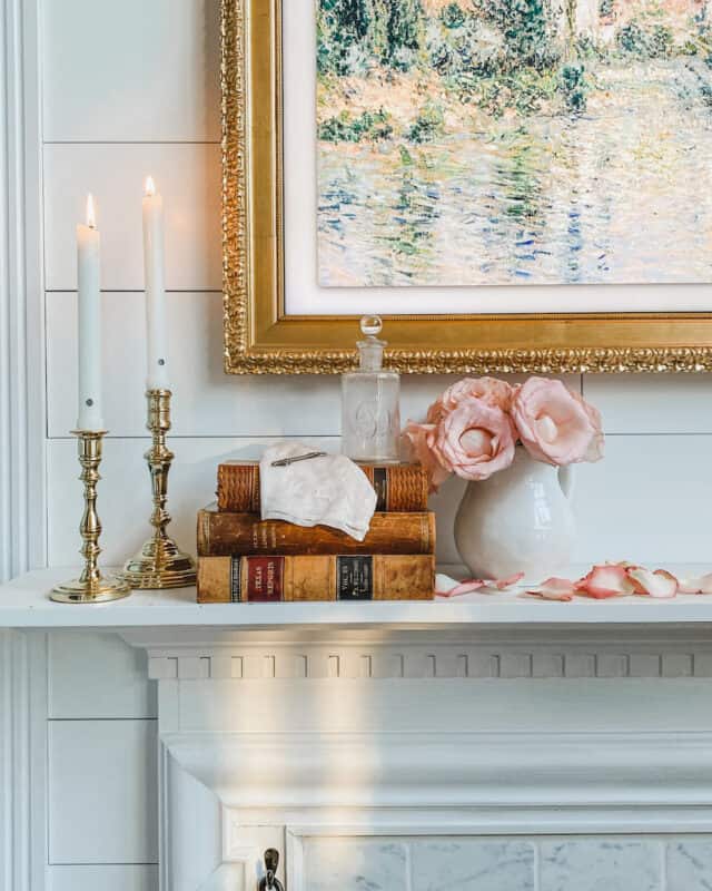 a very romantic valentine' day mantel with two taper candles, antique books and an ironstone pitcher with pink roses in it.