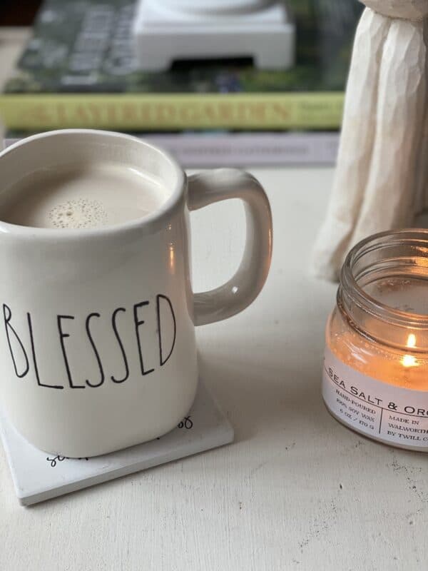 coffee cup filled with coffee on and end table with a lit candle and spring decor