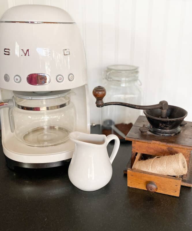 SMEG coffee maker on countertop with a vintage creamer and coffee grinder in the picture