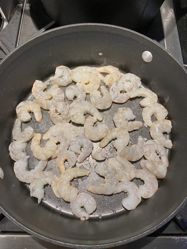 Shrimp put in a saute pan in a single layer starting to cook