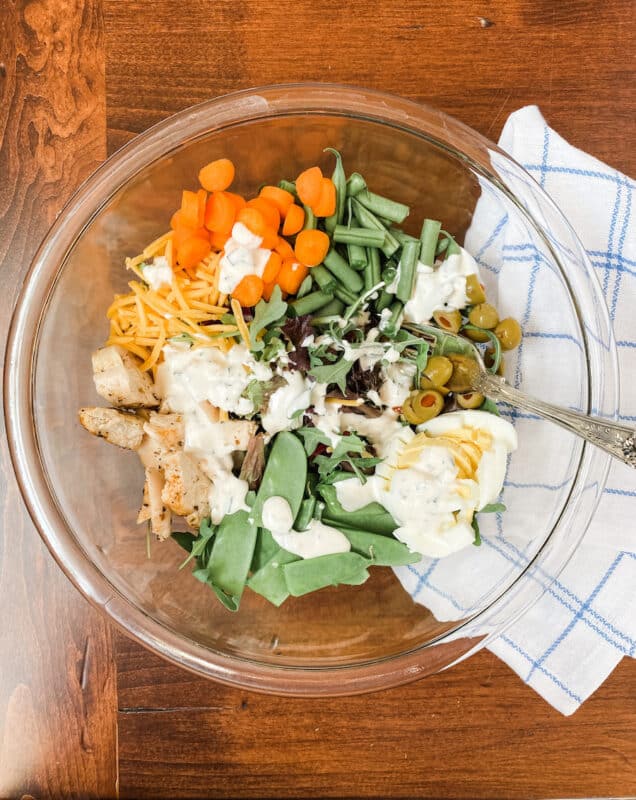 a bowl filled with spring greens and all the fixings for a great spring salad covered with homemade ranch dressing