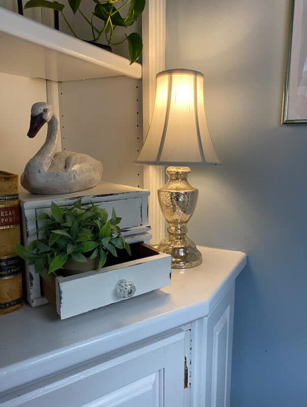 a small table lamp on in the corner of a shelf in the living room. Using mood lighting to refresh for spring