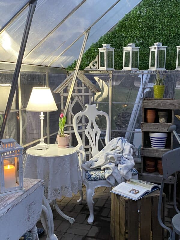 The corner of my greenhouse with the cozy corner with a chair and end table from in the house. It looks so amazing at night with a lamp n the table. 