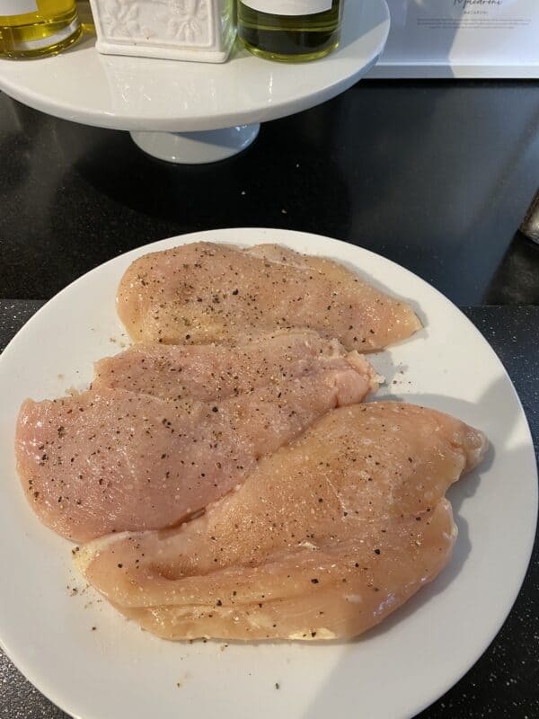 Raw chicken breat on plate with lemon juice and salt and pepper ready for easy creamy chicken marsala