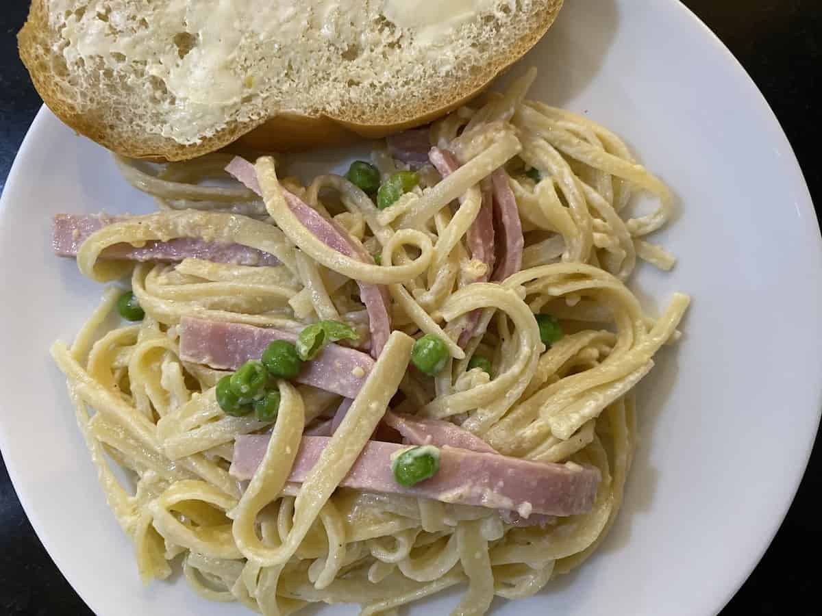 lazy day ham & pea pasta recipe plated on a white plate with a slice of French buttered bread