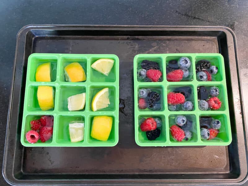 silicone ice cube trays with berries and water on a baking sheet. one of my 7 essential kitchen ice cube recipe
