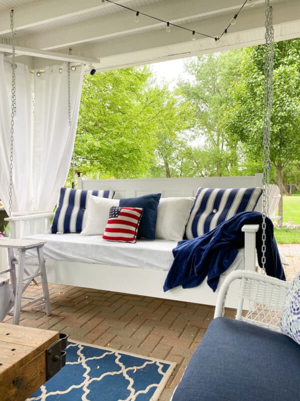 white outdoor swing bed with blue and white pillows and one red, white, and blue flag pillow for simple patriotic decor