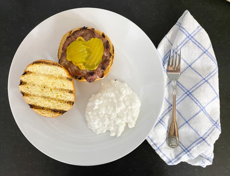 turkey burger on a plate with yellow mustard, burger dill pickles and a side of cottage cheese