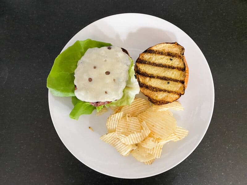 turkey burger on a bun with lettuce and Swiss cheese, potato chips on the side
