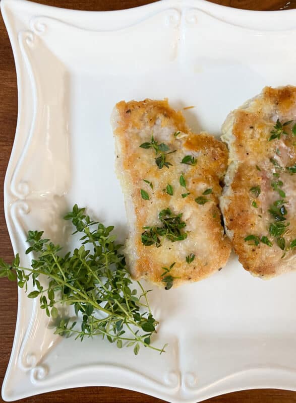 gluten-free cheese-crusted pork chops plated on a white platter with fresh thyme garnish