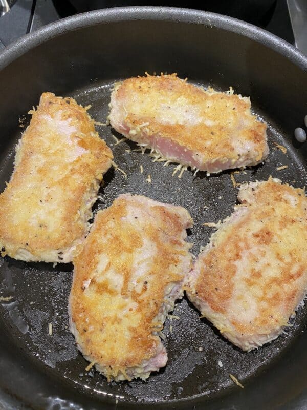 gluten-free cheese-crusted pork chops sautéing in a skillet to brown both sides