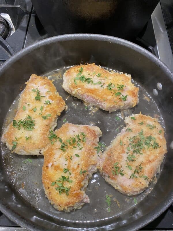 gluten-free cheese-crusted pork chops with lemon and chicken broth in a skillet. It's ready to simmer