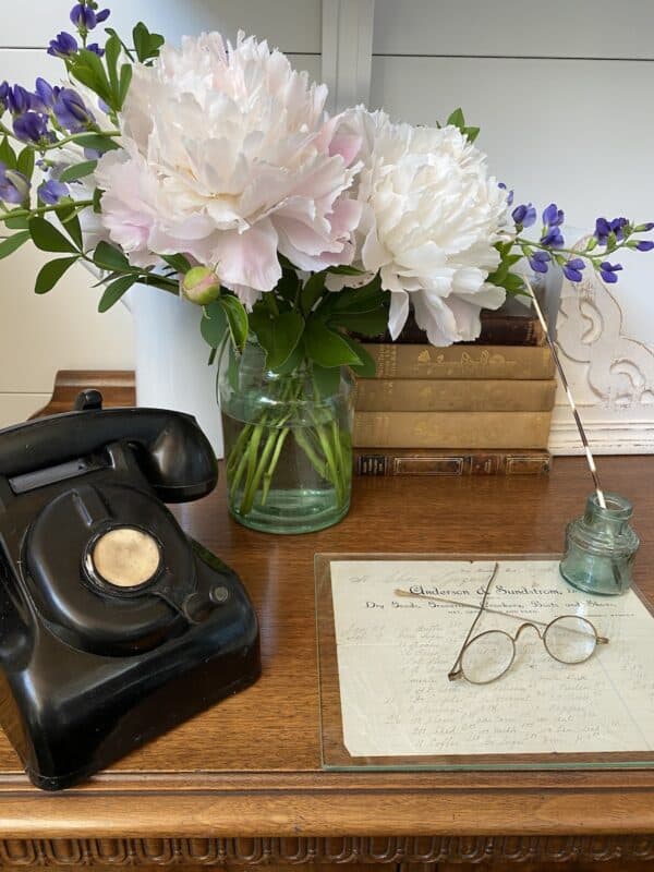 picture of peony flowers in a vase on my sideboard along with a vintage phone, vintage books, and a few other vintage items.