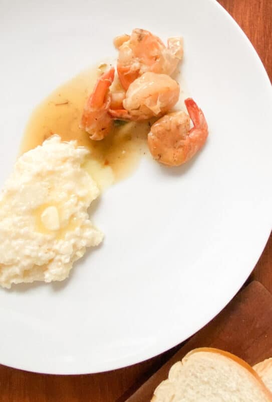 white plate with grits and shrimp in cajun butter sauce