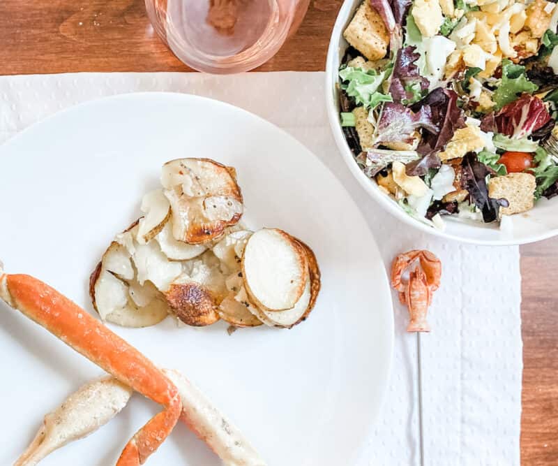 a picture of foil packet potatoes, crab legs and a side salad on the table