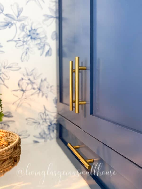 picture that highlights the beautiful blue and white wallpaper, the blue cabinets and the brass hardware