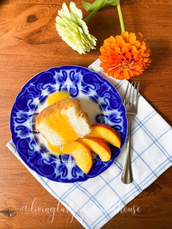 flow blue plate with angel food cake topped with peach syrup and peach slices on the side