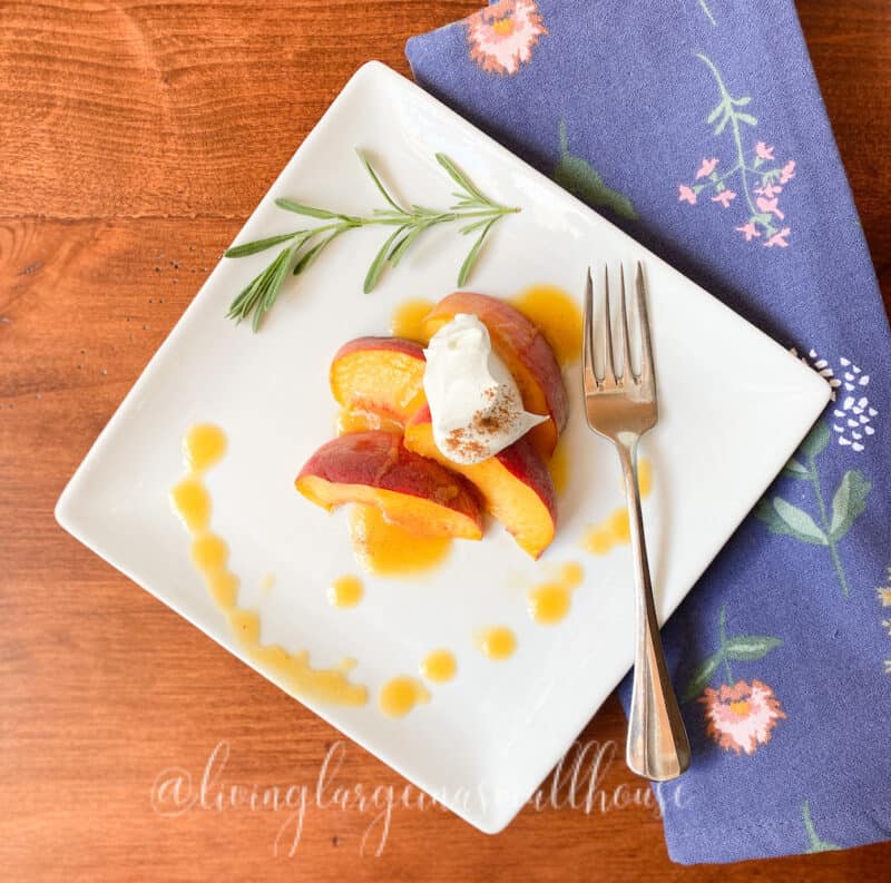 peaches on a white plate topped with peach syrup, whipped cream and cinnamon
