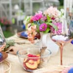 outdoor tablescape with bowl of fruit, fresh flowers and rose gold table settings
