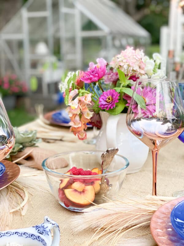 outdoor tablescape with bowl of fruit, fresh flowers and rose gold table settings