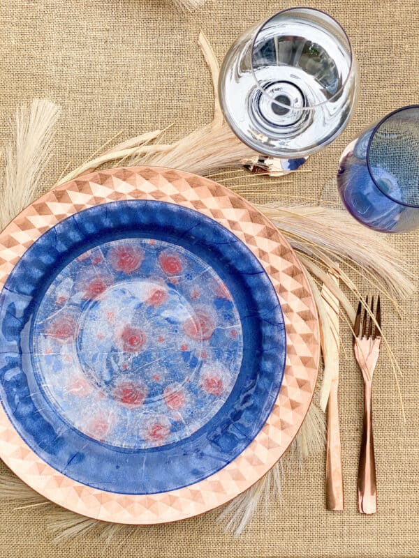 a place setting with a rose gold charger, navy blue napkin decoupaged dinner plate and a peach and blue floral decoupaged salad plate