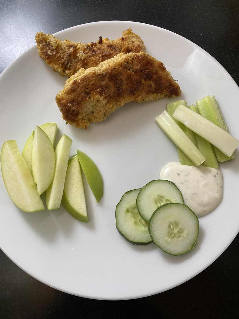 gluten-free chicken strips plated with ranch dressing dip, apple slices and raw vegetables.
