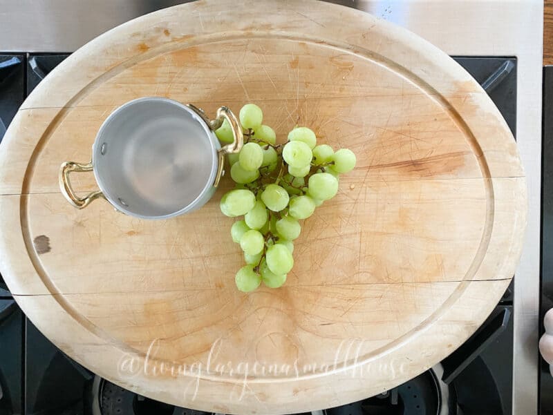 cutting board with a bunch of grapes in the middle and a stainless bowl to start