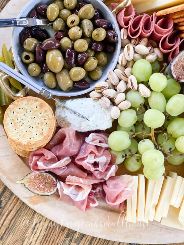 overview of a board with meats, cheese, olives and grapes.