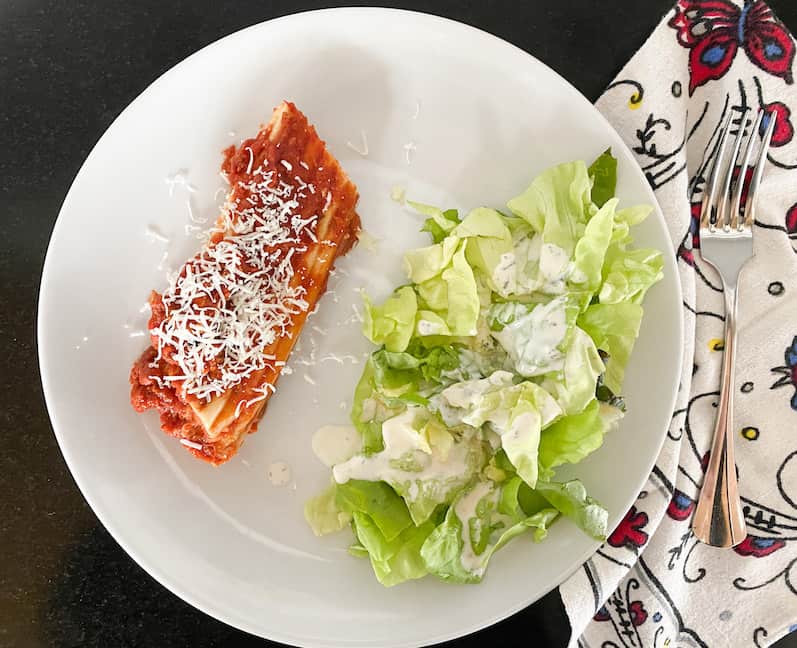 white plate with cheesy manicotti and a side salad