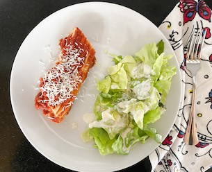 white plate with cheesy manicotti and a side salad